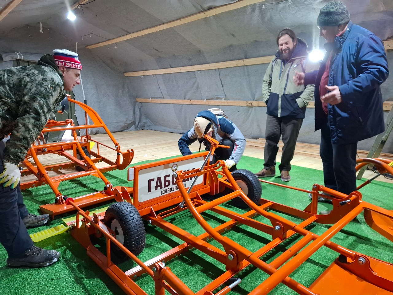 Мария Поселова В цеху по сборке Габоши: представитель Москомспорта и сети лыжных комплексов Москвы - Алексей Гурбанов и директор лыжного комплекса в Алешкино - Дмитрий Калинкин изучают конструкцию новой Габоши. Декабрь 2025. На фото слева направо: Александр Репетуха, Дмитрий Калинкин, Алексей Гурбанов, Геннадий Фищенко.