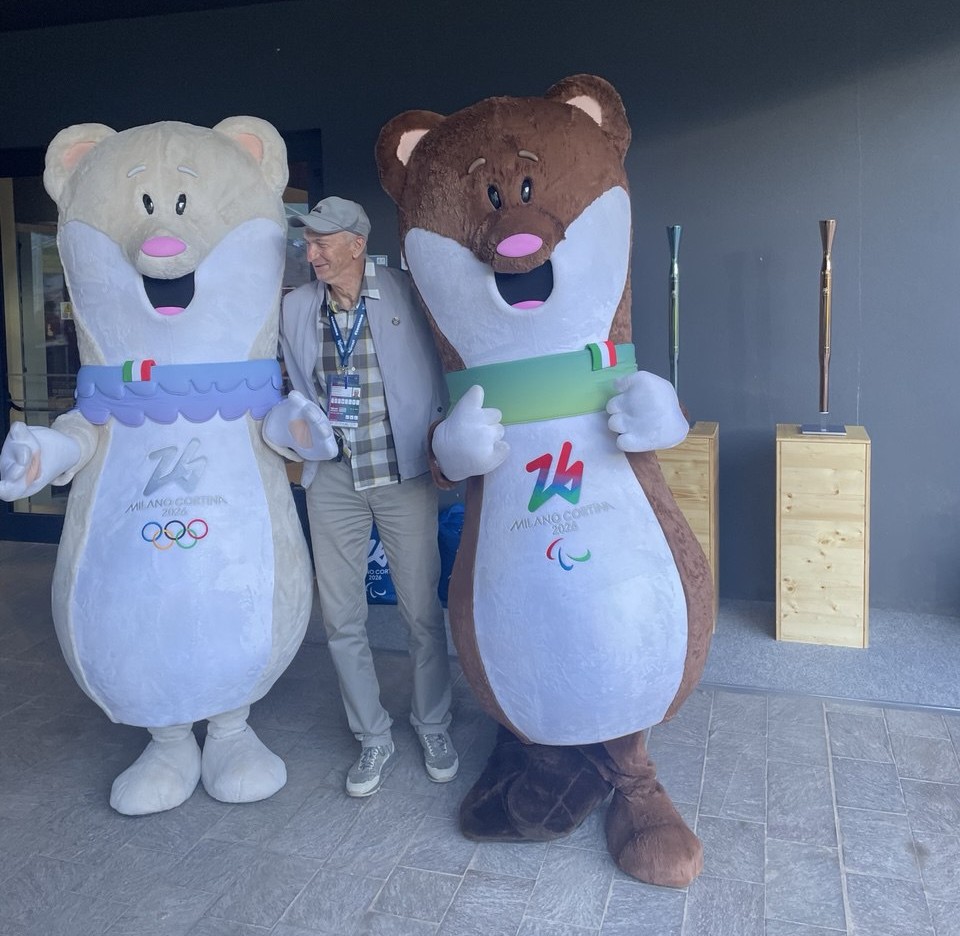 skisport.ru Талисманы Олимпийских и Паралимпийских Игр 2026. На заднем плане факелы для эстафеты олимпийского огня.