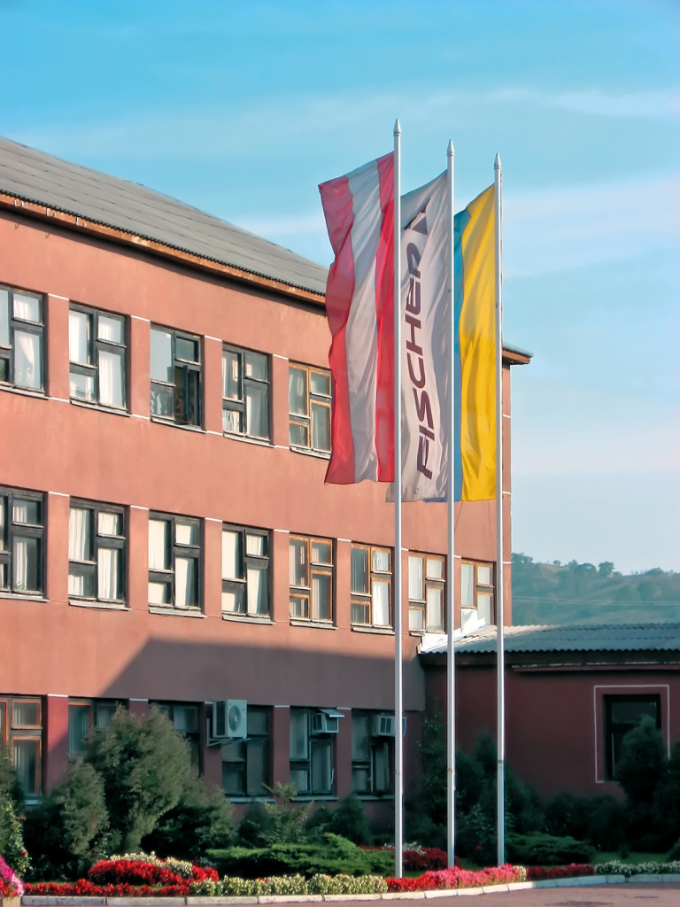 У центрального входа на фабрику развеваются три флага с государственные флаги Австрии и Украины, а также флаг компании FISCHER.